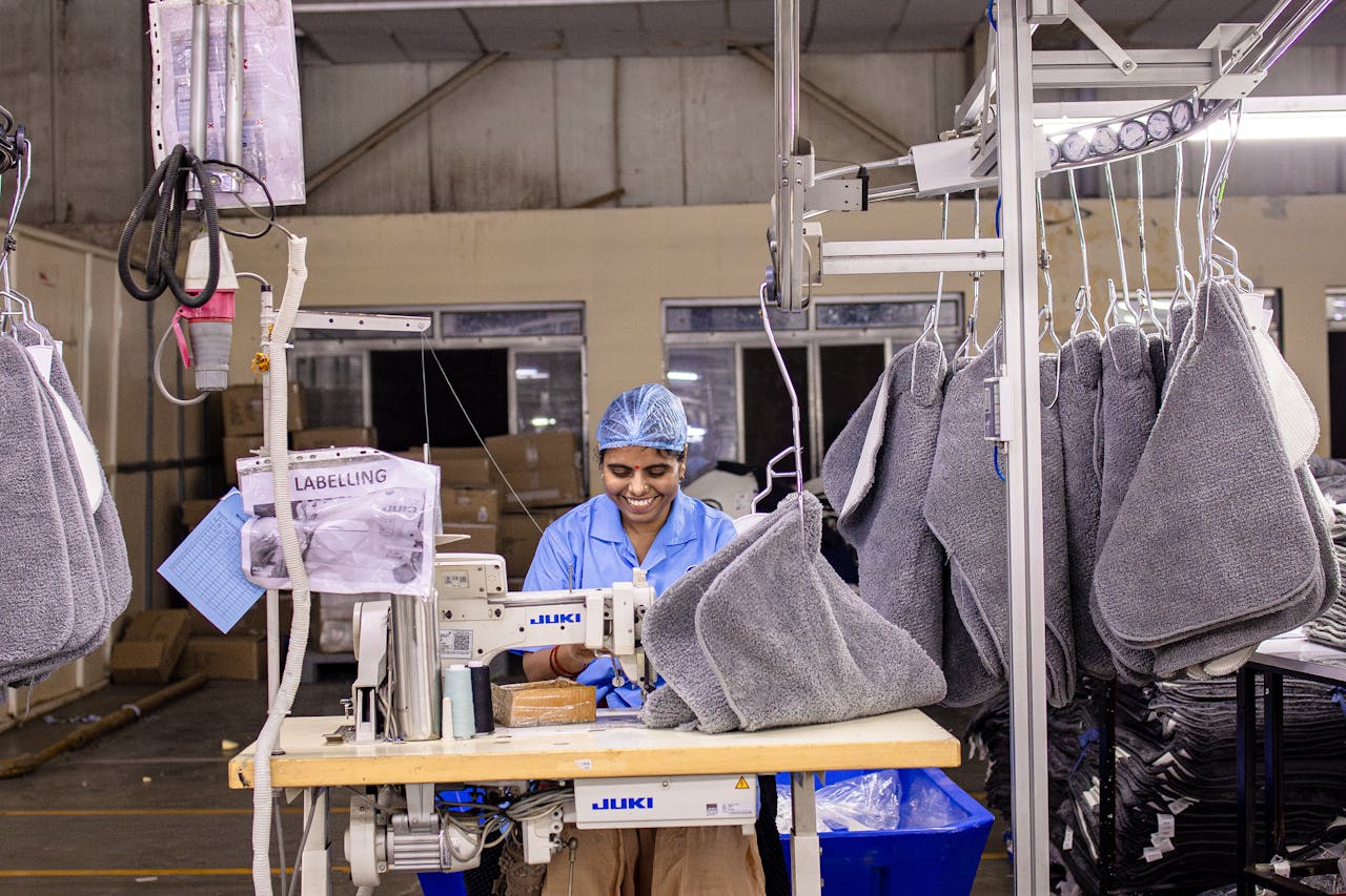 A factory worker sewing textiles on an industrial machine in a modern garment manufacturing facility.