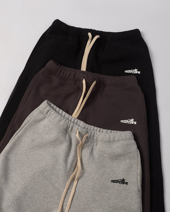 Three neatly stacked pairs of sweatpants with drawstrings in stylish neutral colors.