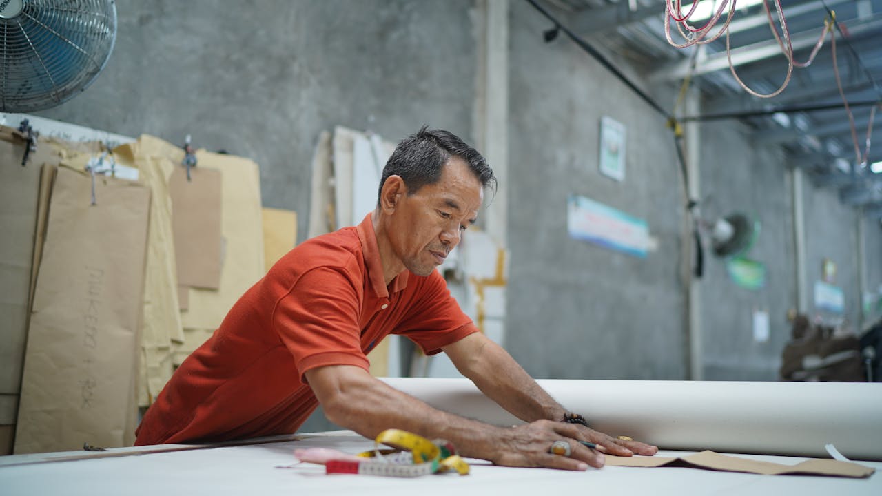 Asian man carefully crafting patterns in a traditional tailor workshop.