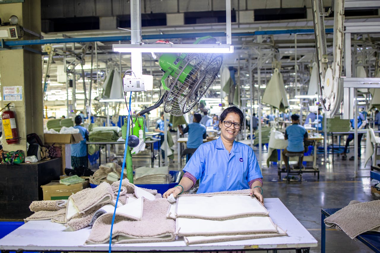 A textile worker smiles while handling fabrics in a bustling factory setting, showcasing industrial culture.