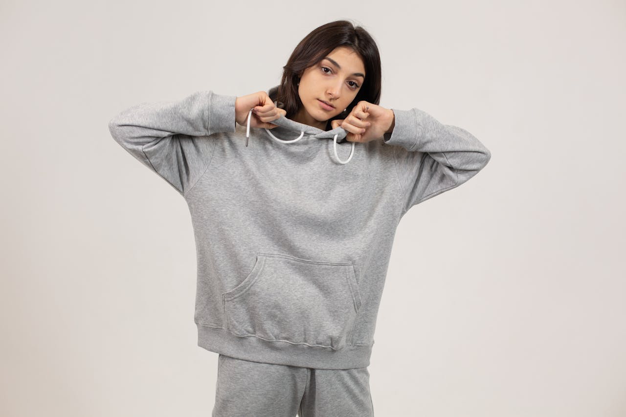 Serious female wearing oversize hoodie and sweatpants standing against white background and looking at camera